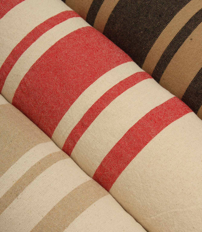 Angled display of coordinating striped fabrics featuring warm earthy shades, textured woven finishes, and timeless stripe patterns suitable for upholstery and curtains.