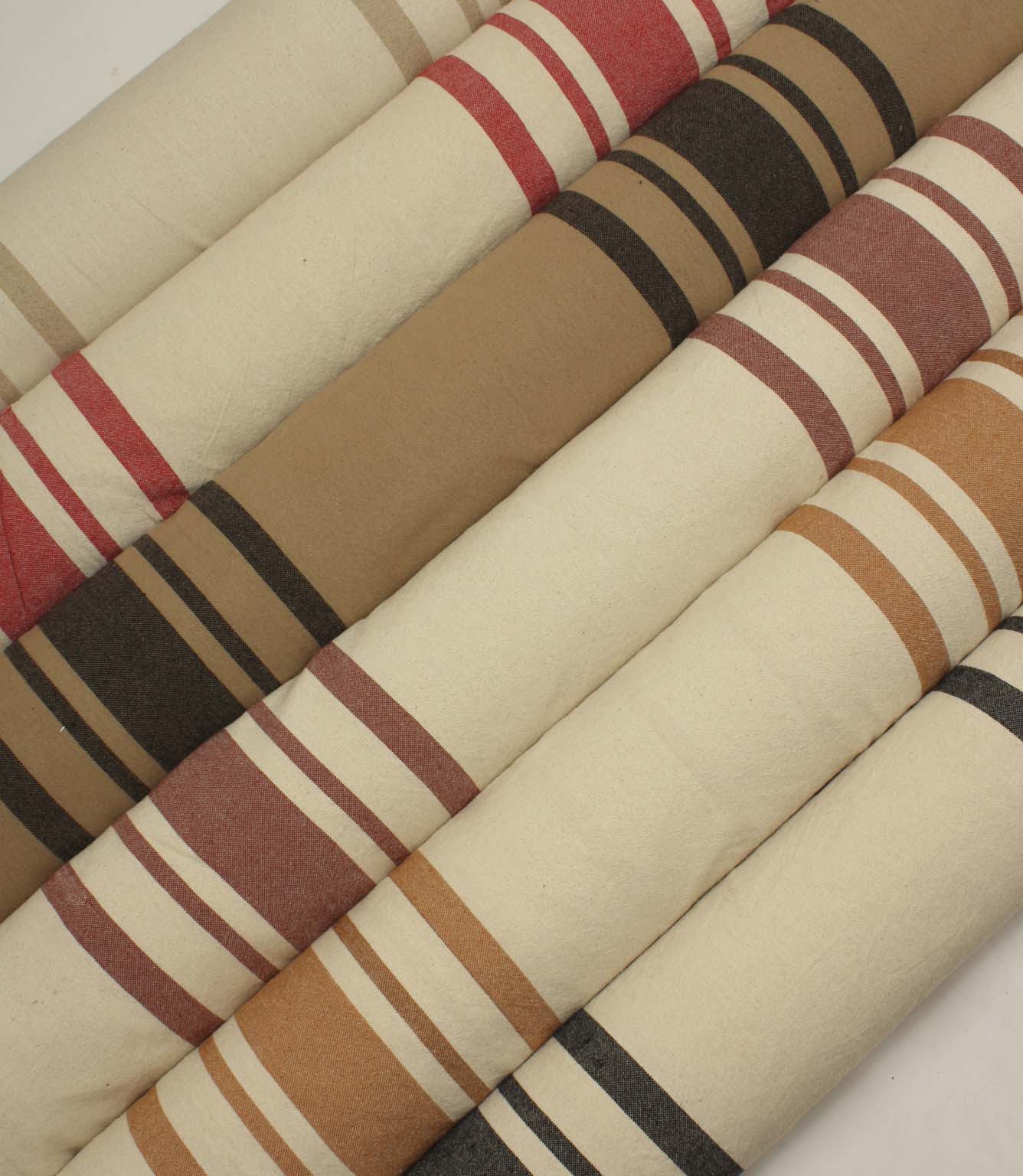 Collection of striped upholstery and curtain fabrics arranged in horizontal rolls, showcasing classic woven stripe designs in soft neutral and earthy tones.