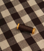 Brown and ivory checked fabric displayed with matching thread spool for colour reference.