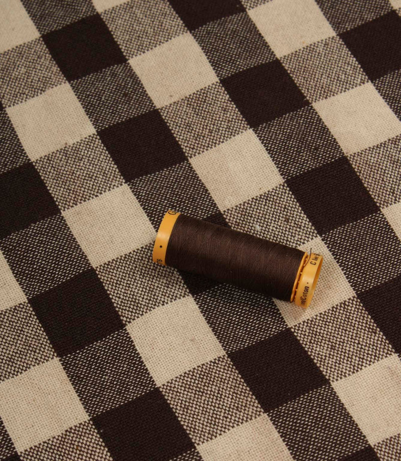 Brown and ivory checked fabric displayed with matching thread spool for colour reference.