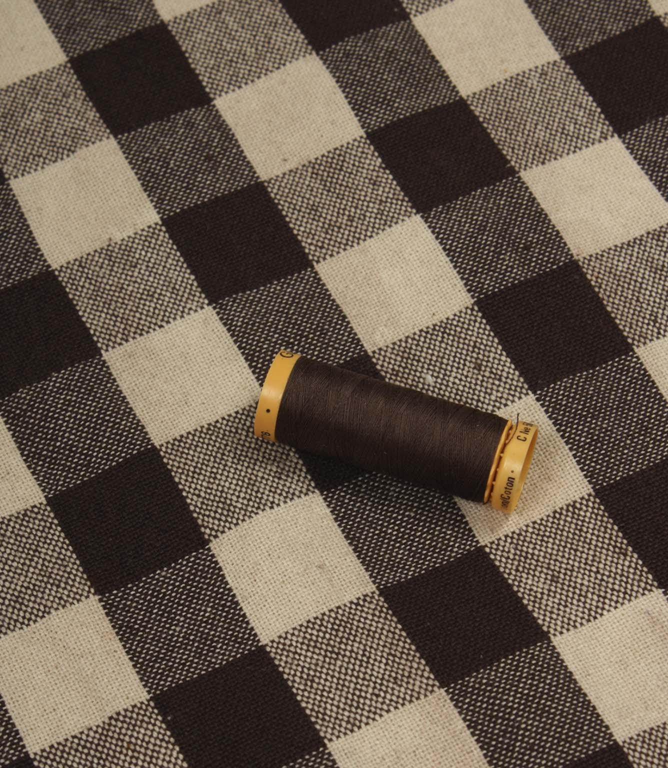 Brown and ivory checked fabric displayed with matching thread spool for colour reference.