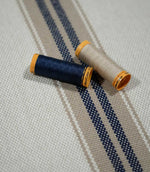 Alma Stripe Marina woven striped fabric styled with navy and natural thread spools, highlighting the textured weave and coordinating stripe design.