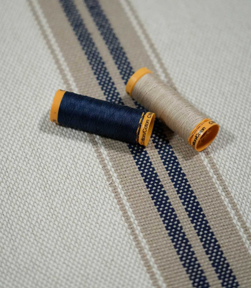 Alma Stripe Marina woven striped fabric styled with navy and natural thread spools, highlighting the textured weave and coordinating stripe design.