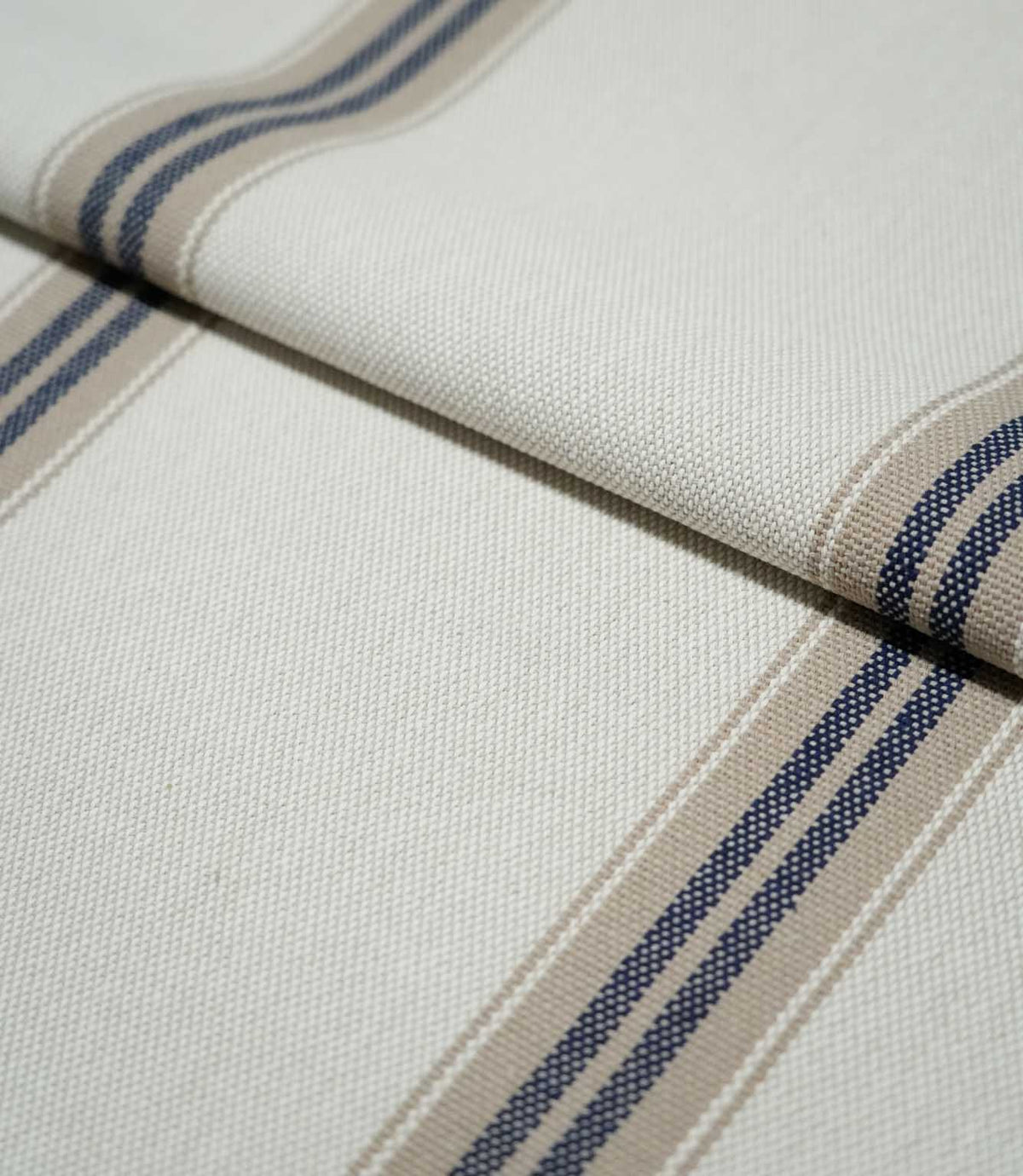 Folded Alma Stripe Marina fabric showing the off-white woven ground with repeating navy blue and natural beige stripes and a tactile textured finish.