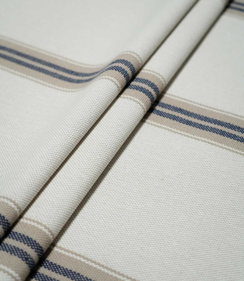 Alma Stripe Marina woven fabric arranged in soft folds, showing the widely spaced navy blue and beige stripe pattern across the off-white ground.