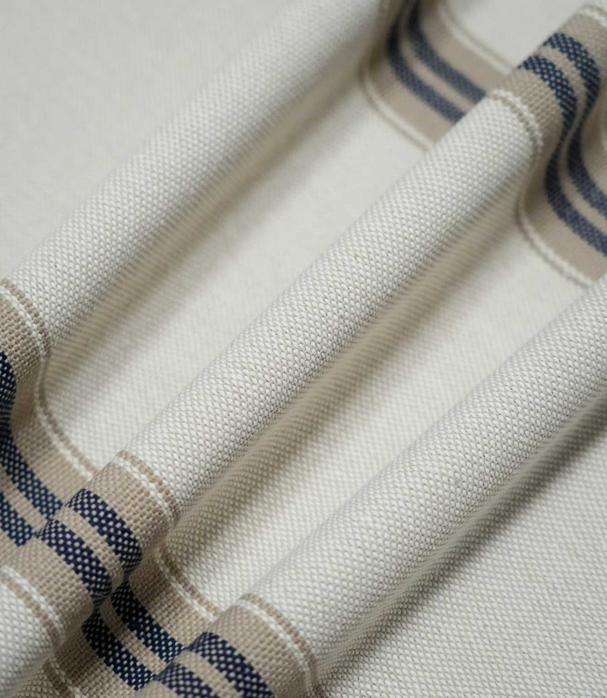 Close-up of Alma Stripe Marina fabric draped in soft folds, highlighting the substantial woven texture and repeating navy blue and natural beige stripes.