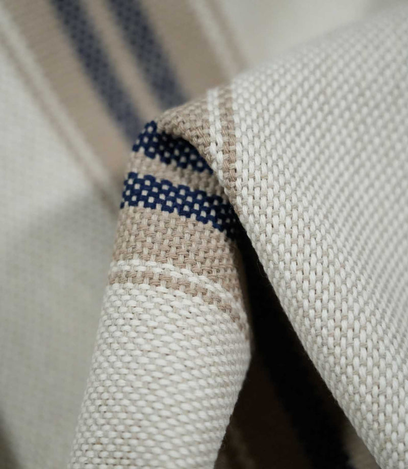 Macro close-up of folded Alma Stripe Marina fabric showing the detailed off-white weave and navy blue stripes set within a natural beige band.