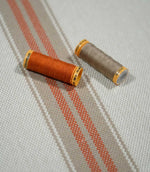 Alma Stripe Terracotta woven striped fabric styled with terracotta and natural thread spools, highlighting the coordinating colours and textured weave.