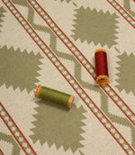 Sage green geometric patterned fabric laid flat with coordinating green and red thread spools, highlighting the upholstery-weight weave and Southwestern-inspired design.