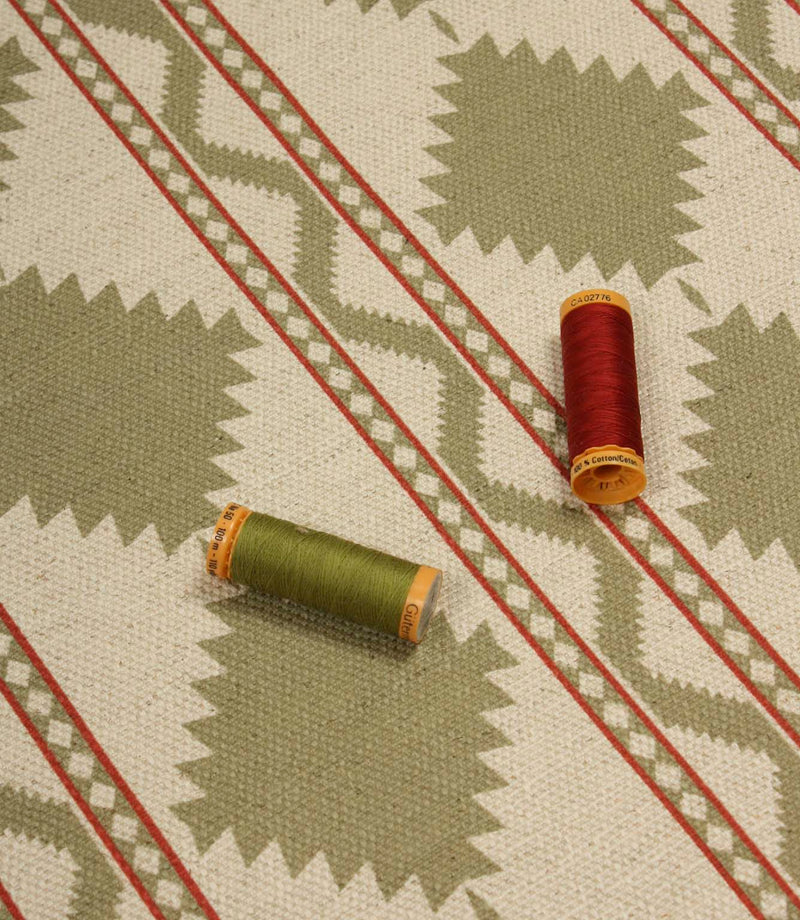 Sage green geometric patterned fabric laid flat with coordinating green and red thread spools, highlighting the upholstery-weight weave and Southwestern-inspired design.