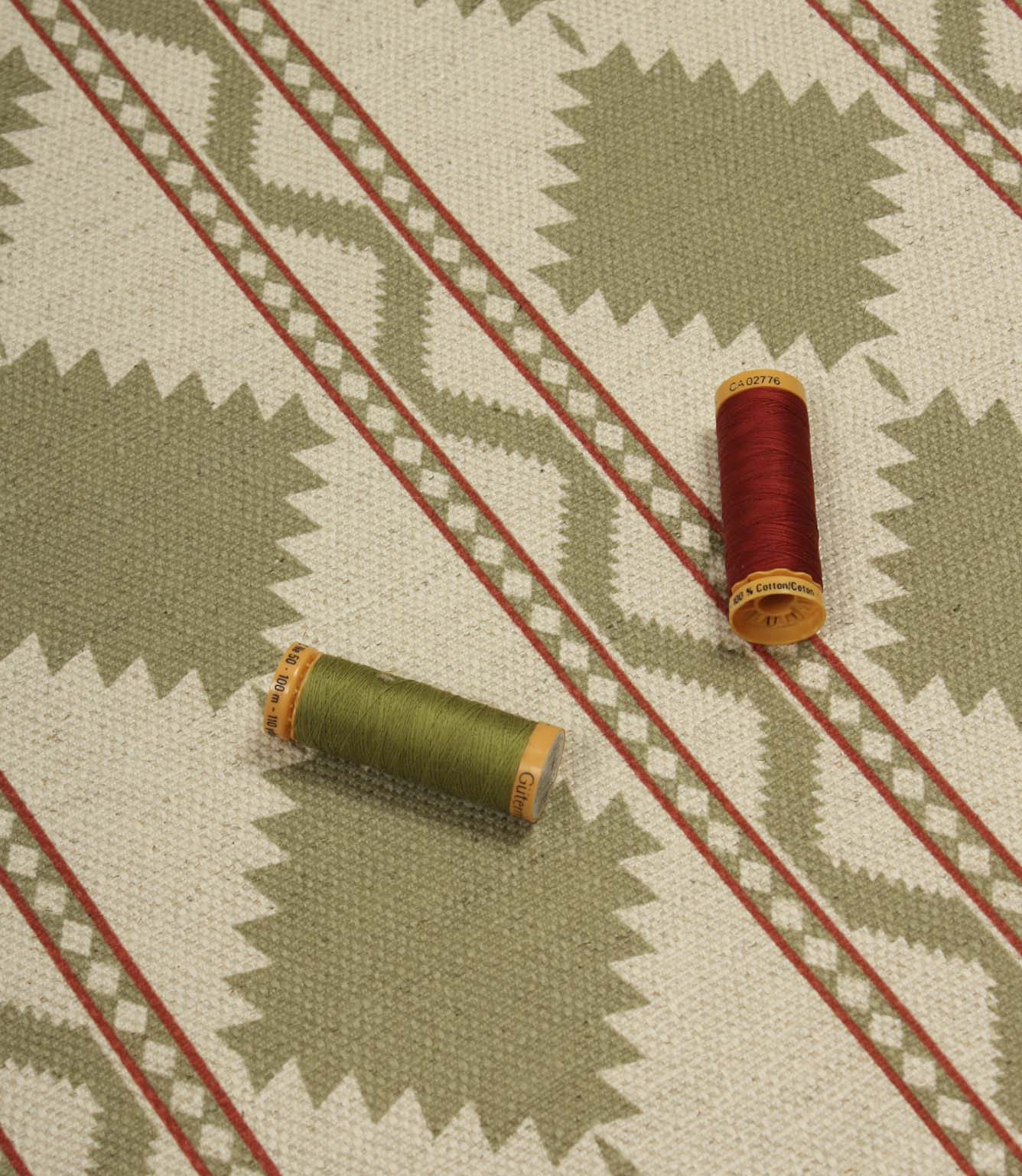 Sage green geometric patterned fabric laid flat with coordinating green and red thread spools, highlighting the upholstery-weight weave and Southwestern-inspired design.