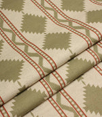Folded sage green geometric fabric showcasing the structured drape and repeating tribal-style diamond pattern with red stripe accents.