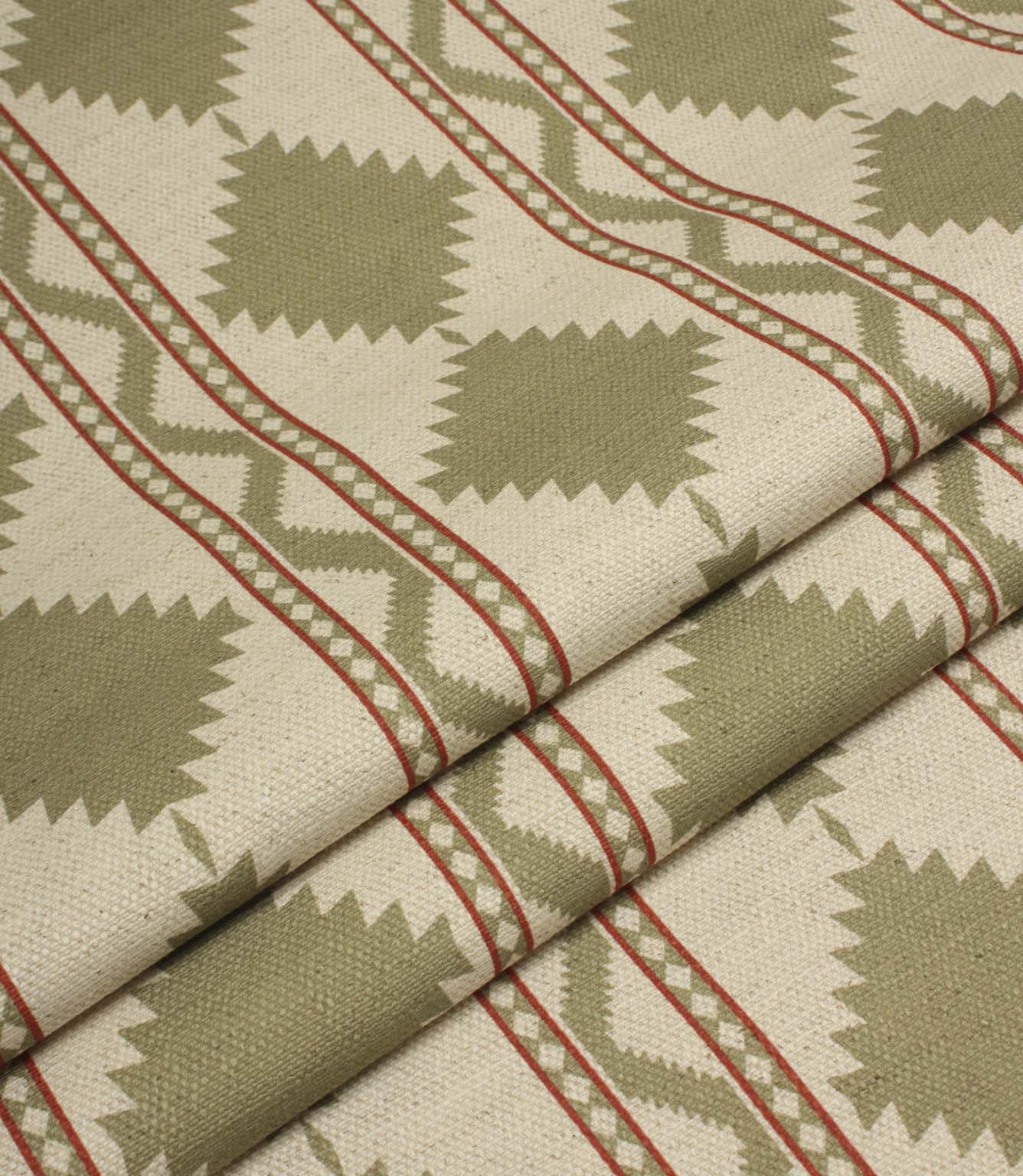 Folded sage green geometric fabric showcasing the structured drape and repeating tribal-style diamond pattern with red stripe accents.