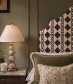 Arlo Geo Azure fabric upholstered statement headboard featuring a navy geometric floral stripe pattern on a natural background with burgundy piping, styled with layered cushions and a bedside lamp.