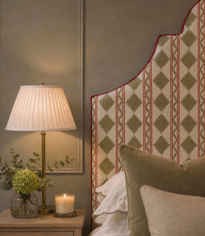 Arlo Geo Olive fabric upholstered statement headboard with repeating olive geometric motifs and red striped detailing on a natural background, finished with red piping and styled with neutral bedding.