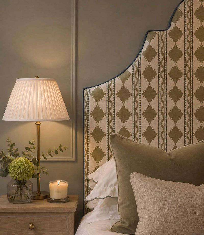 Arlo Geo Olive fabric upholstered headboard featuring repeating olive geometric motifs and striped detailing on a natural background, finished with contrasting blue piping and styled with olive and neutral cushions.