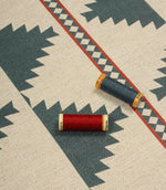 Southwestern-inspired patterned fabric displayed with coordinating thread reels, featuring large teal diamond motifs on a natural cream background.