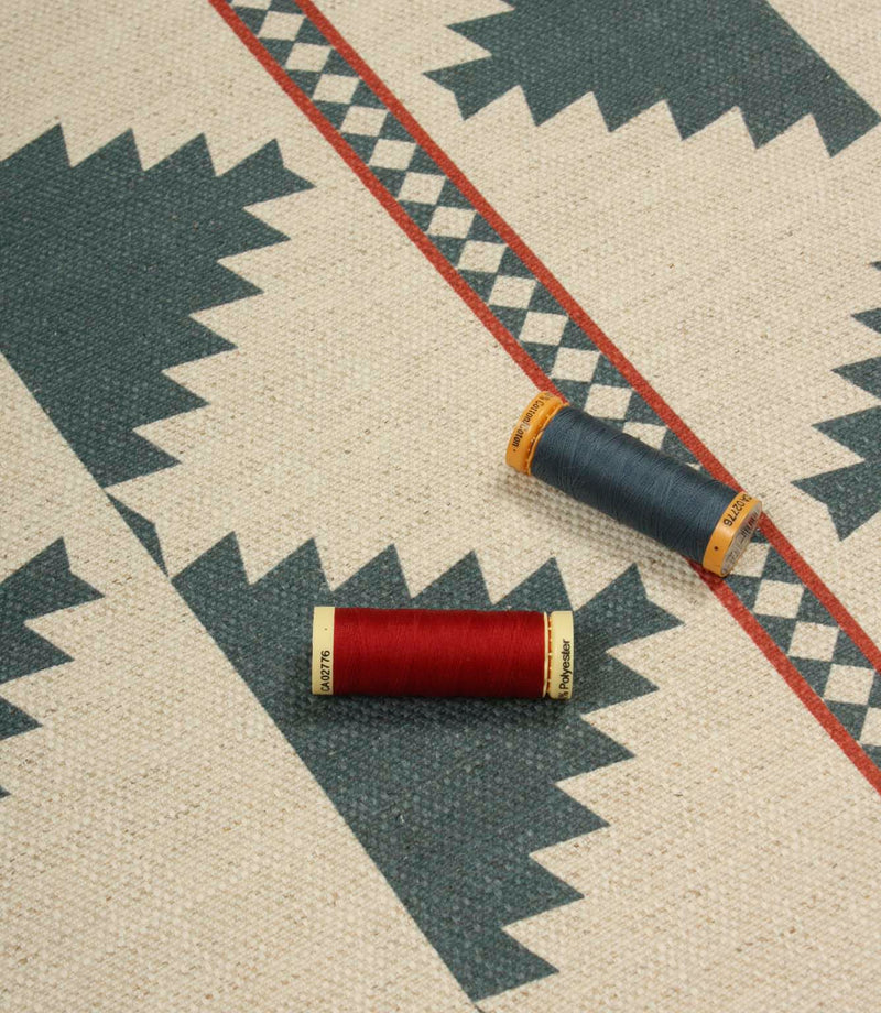Southwestern-inspired patterned fabric displayed with coordinating thread reels, featuring large teal diamond motifs on a natural cream background.