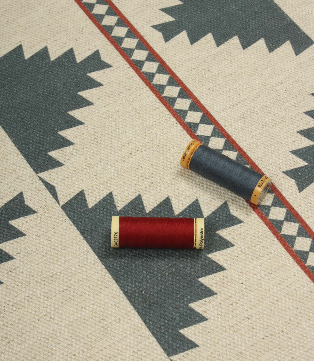 Southwestern-inspired patterned fabric displayed with coordinating thread reels, featuring large teal diamond motifs on a natural cream background.