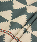 Folded cream and teal geometric fabric showing the bold repeating pattern, decorative border detail, and soft textured finish.