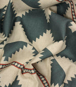 Draped tribal-style furnishing fabric with oversized teal diamond motifs and rust red accents on a natural woven background.