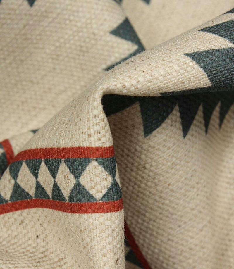 Macro close-up of cream woven fabric highlighting the textured weave, teal geometric border pattern, and rust red accent stripes.