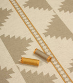 Southwestern-style furnishing fabric displayed with coordinating thread reels, featuring muted taupe diamond motifs on a natural cream woven background.