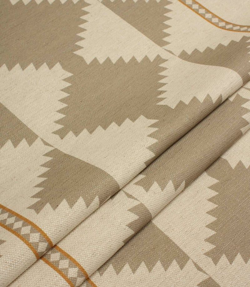 Folded cream and taupe geometric fabric showing the repeating tribal-inspired pattern, decorative border stripes, and textured woven finish.