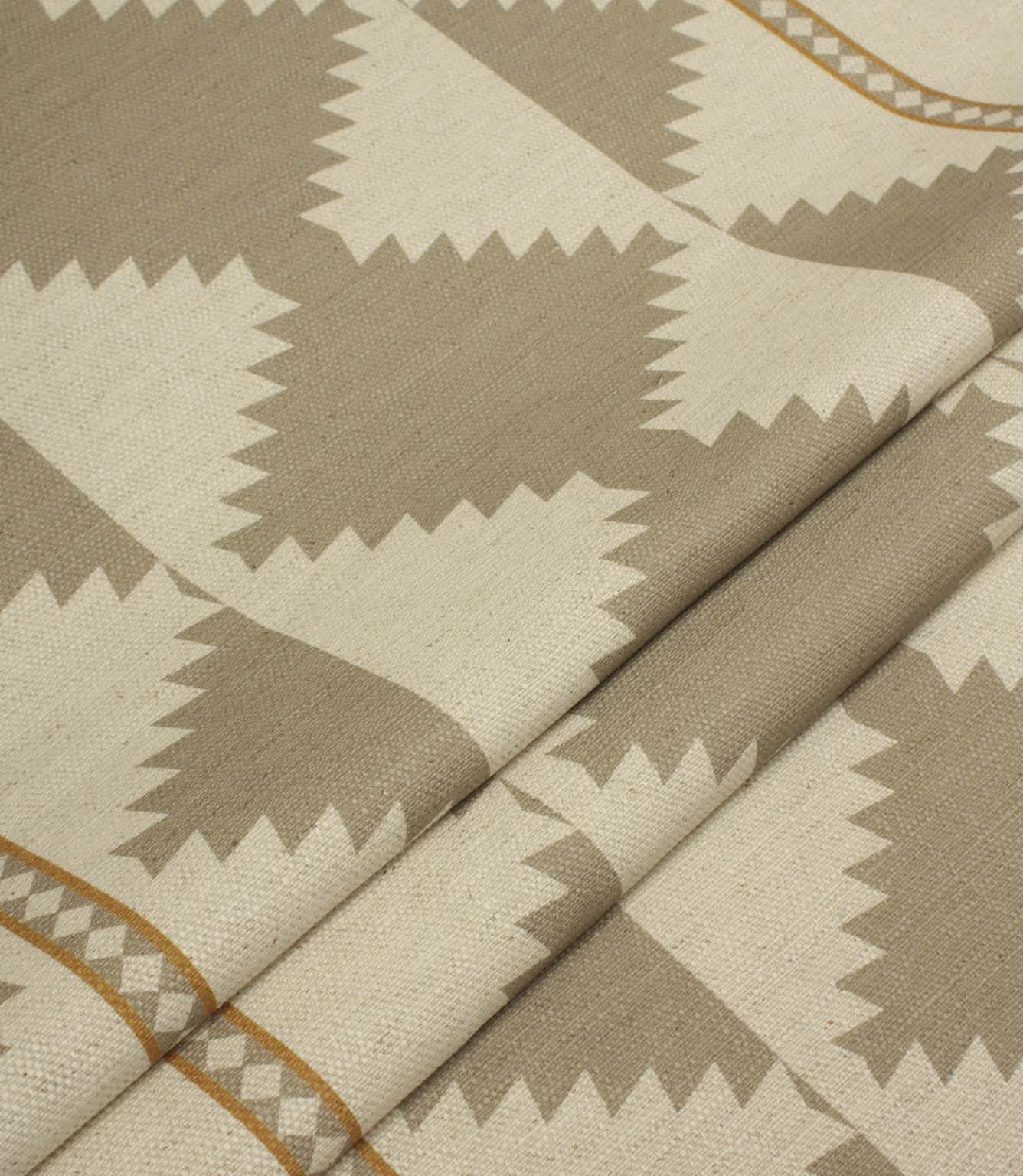 Folded cream and taupe geometric fabric showing the repeating tribal-inspired pattern, decorative border stripes, and textured woven finish.