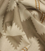 Macro close-up of woven cream fabric highlighting the textured weave, taupe geometric border pattern, and warm ochre accent stripes.