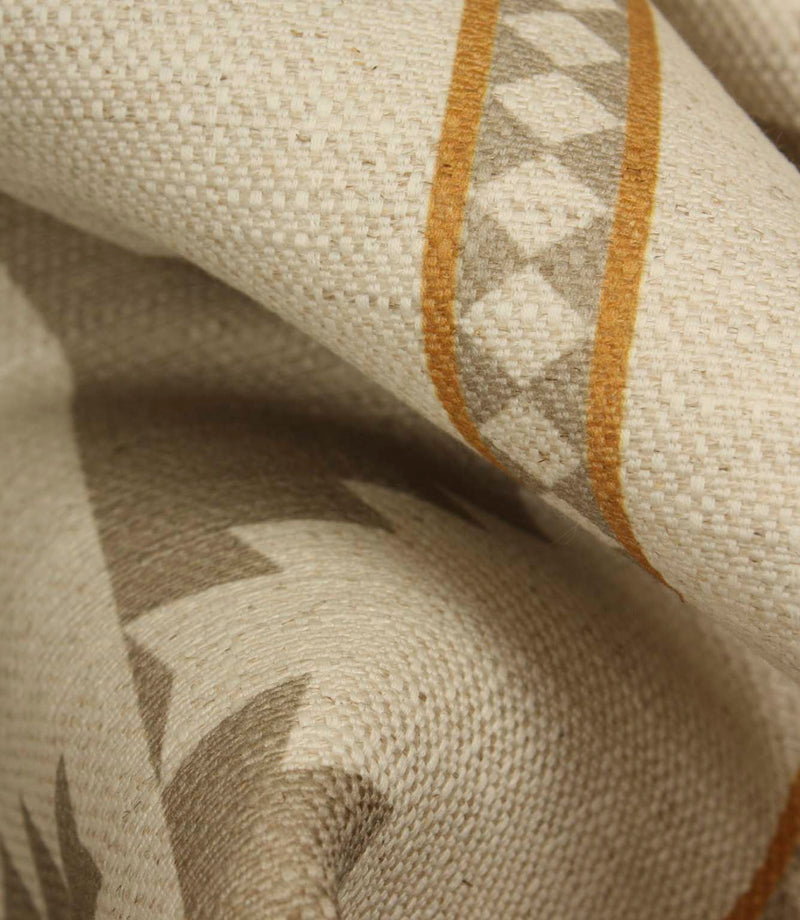 Close-up of cream woven fabric showing the soft drape, textured surface, taupe geometric motif and warm ochre border stripe detail.