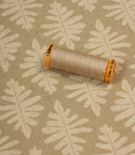 Detailed view of Ashleaf Almond upholstery fabric with thread spool for scale.