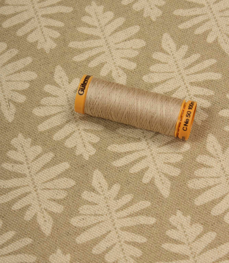 Detailed view of Ashleaf Almond upholstery fabric with thread spool for scale.