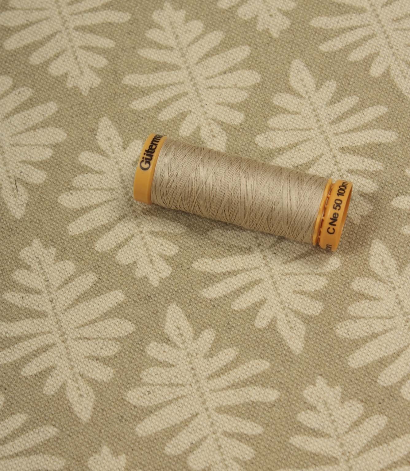 Detailed view of Ashleaf Almond upholstery fabric with thread spool for scale.