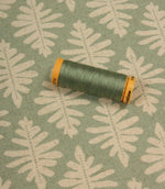 Ashleaf Dill fabric with a coordinating green thread spool highlighting the fabric’s colour and pattern.