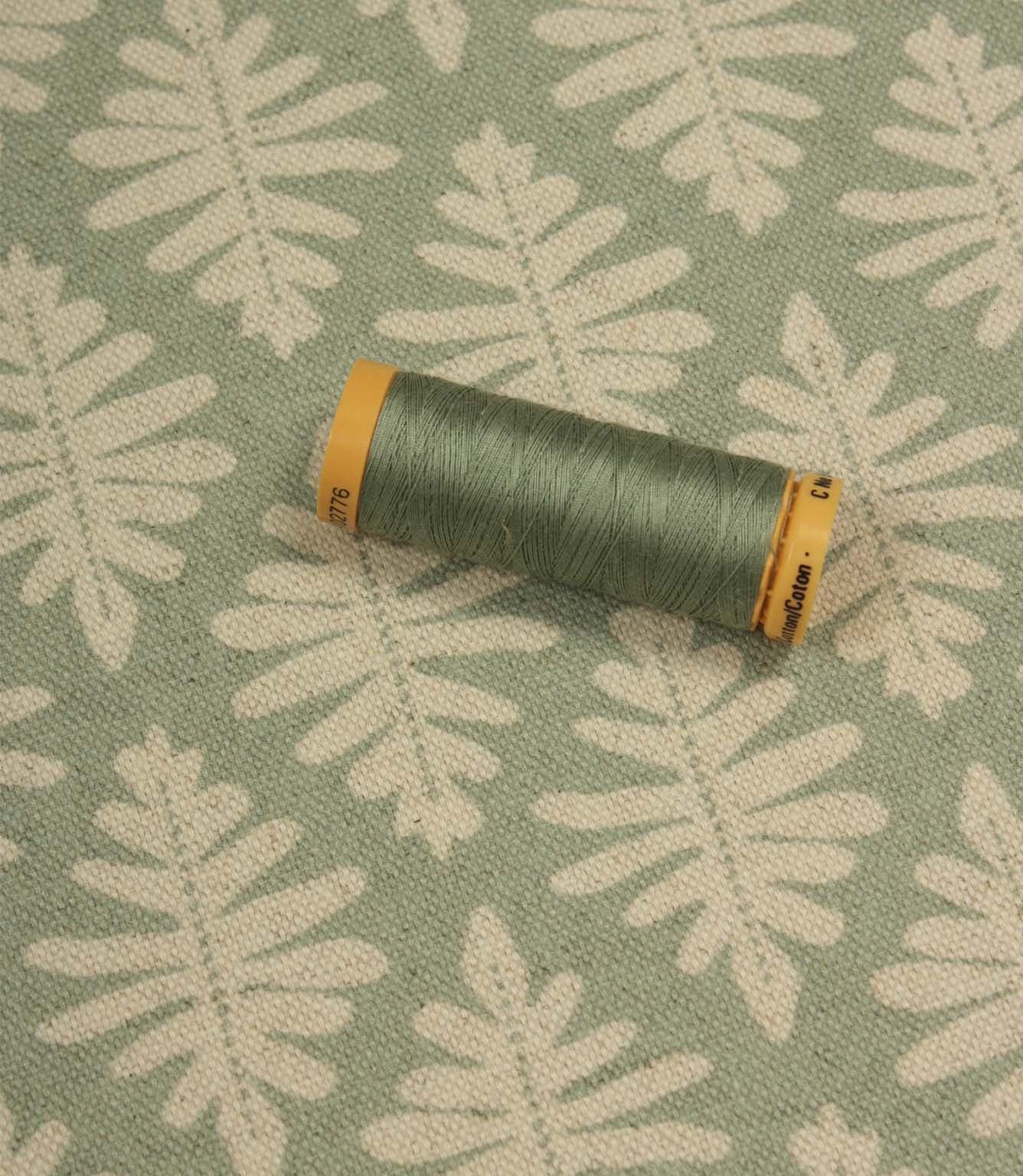 Ashleaf Dill fabric with a coordinating green thread spool highlighting the fabric’s colour and pattern.