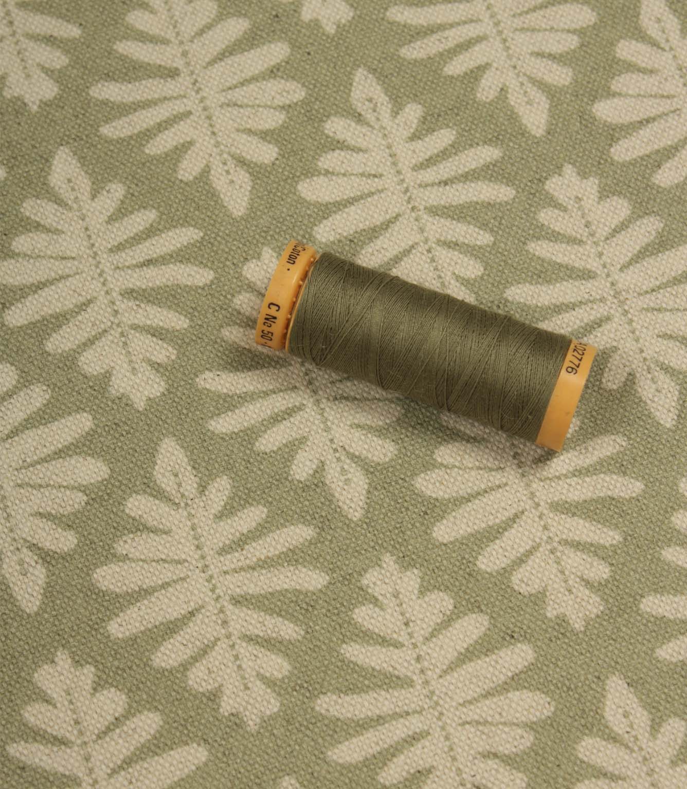 Detailed view of Ashleaf Lemon Grass upholstery fabric with matching thread spool for colour reference and scale.