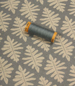 Detailed view of Ashleaf Monsoon upholstery fabric with matching thread spool for colour reference and scale.