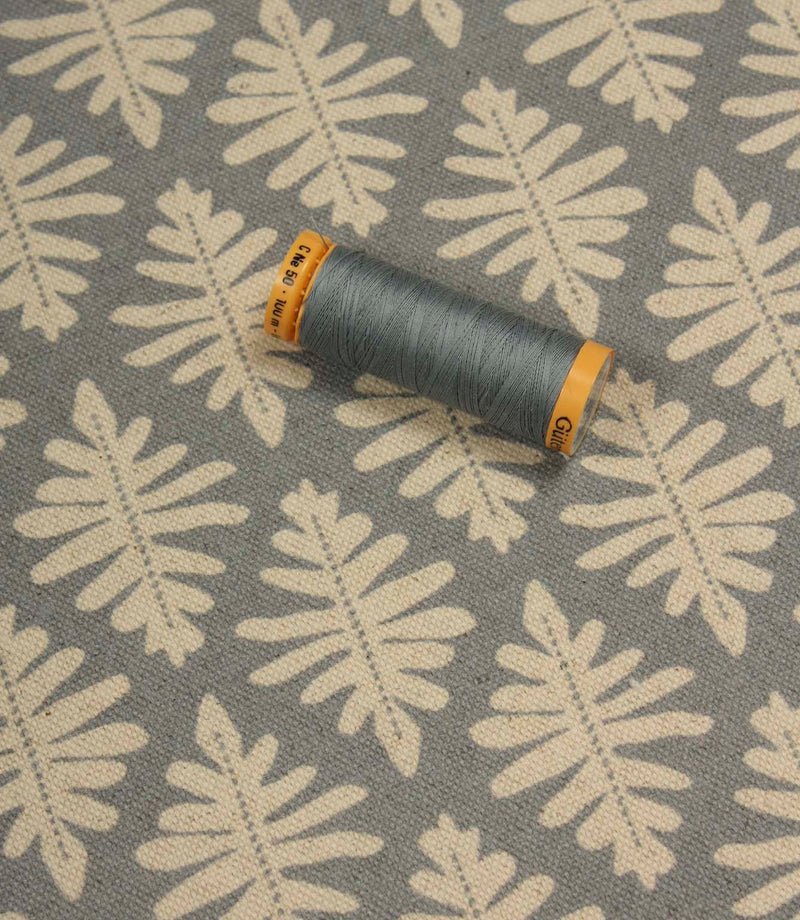 Detailed view of Ashleaf Monsoon upholstery fabric with matching thread spool for colour reference and scale.