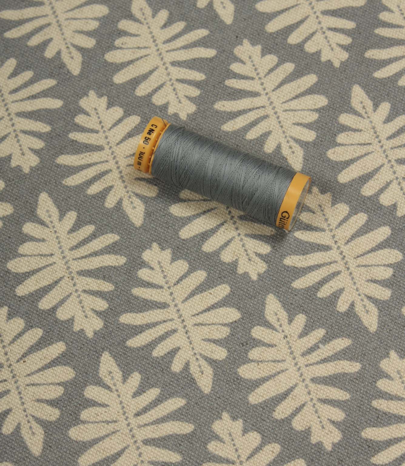 Detailed view of Ashleaf Monsoon upholstery fabric with matching thread spool for colour reference and scale.