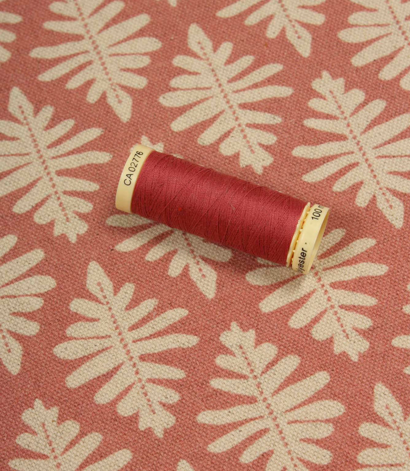 Ashleaf Raspberry fabric displayed with a matching raspberry thread spool, showcasing colour coordination and pattern detail.