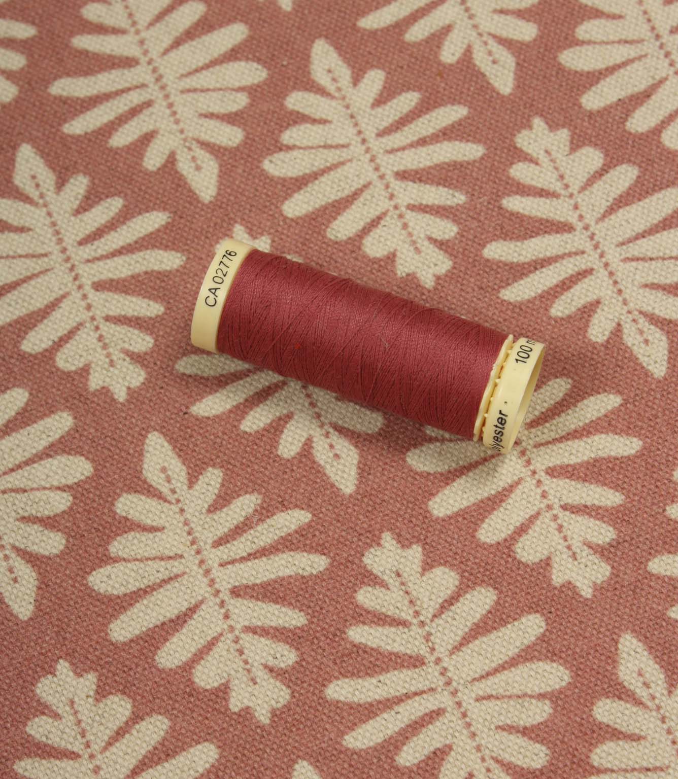 Ashleaf Raspberry fabric displayed with a matching raspberry thread spool, showcasing colour coordination and pattern detail.