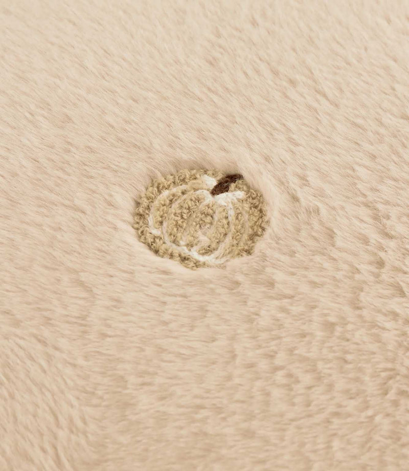 Close-up of a beige embroidered pumpkin motif with a brown stem on the soft natural cream faux fur cushion fabric.