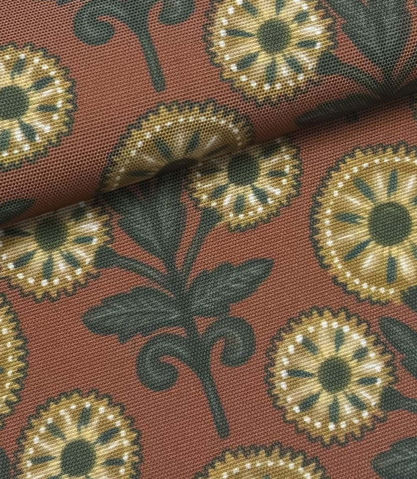 Folded Autumn Sunflower outdoor fabric featuring ochre floral motifs with dark green foliage on a terracotta background.