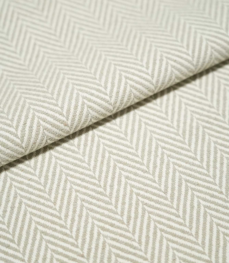 Close-up of folded Bampton Argent herringbone fabric, showing its substantial woven texture, thickness and repeating soft grey and off-white chevron design.