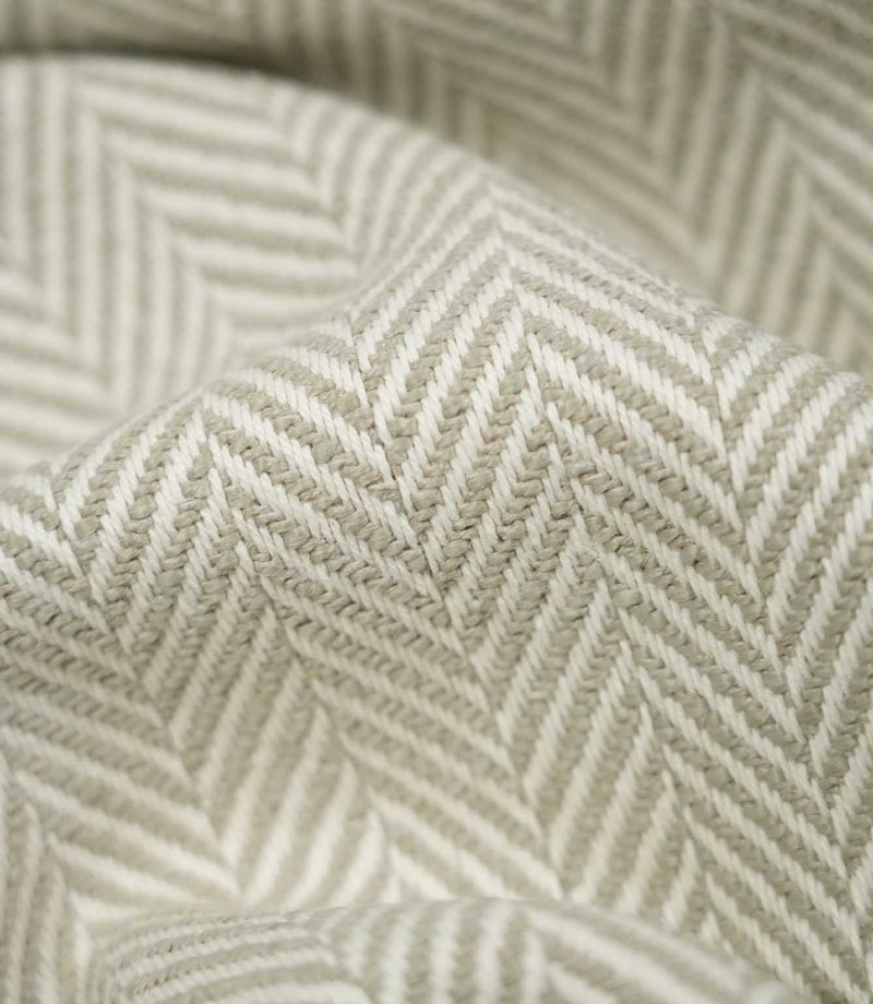 Macro close-up of draped Bampton Argent herringbone fabric, highlighting the individual woven fibres and detailed soft grey-beige and off-white herringbone pattern.