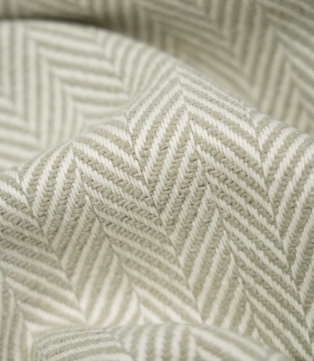 Macro close-up of draped Bampton Argent herringbone fabric, highlighting the individual woven fibres and detailed soft grey-beige and off-white herringbone pattern.