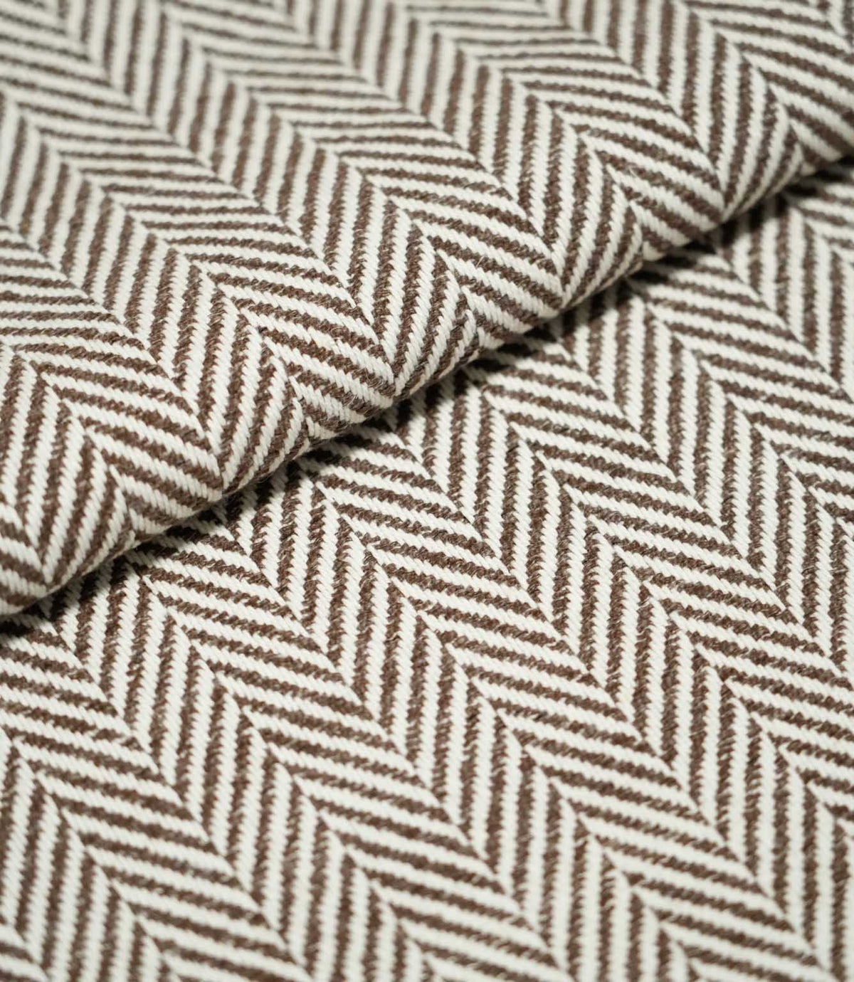 Close-up of folded Bampton Bison herringbone fabric, showing the substantial woven texture, fabric thickness and repeating brown and off-white chevron pattern.