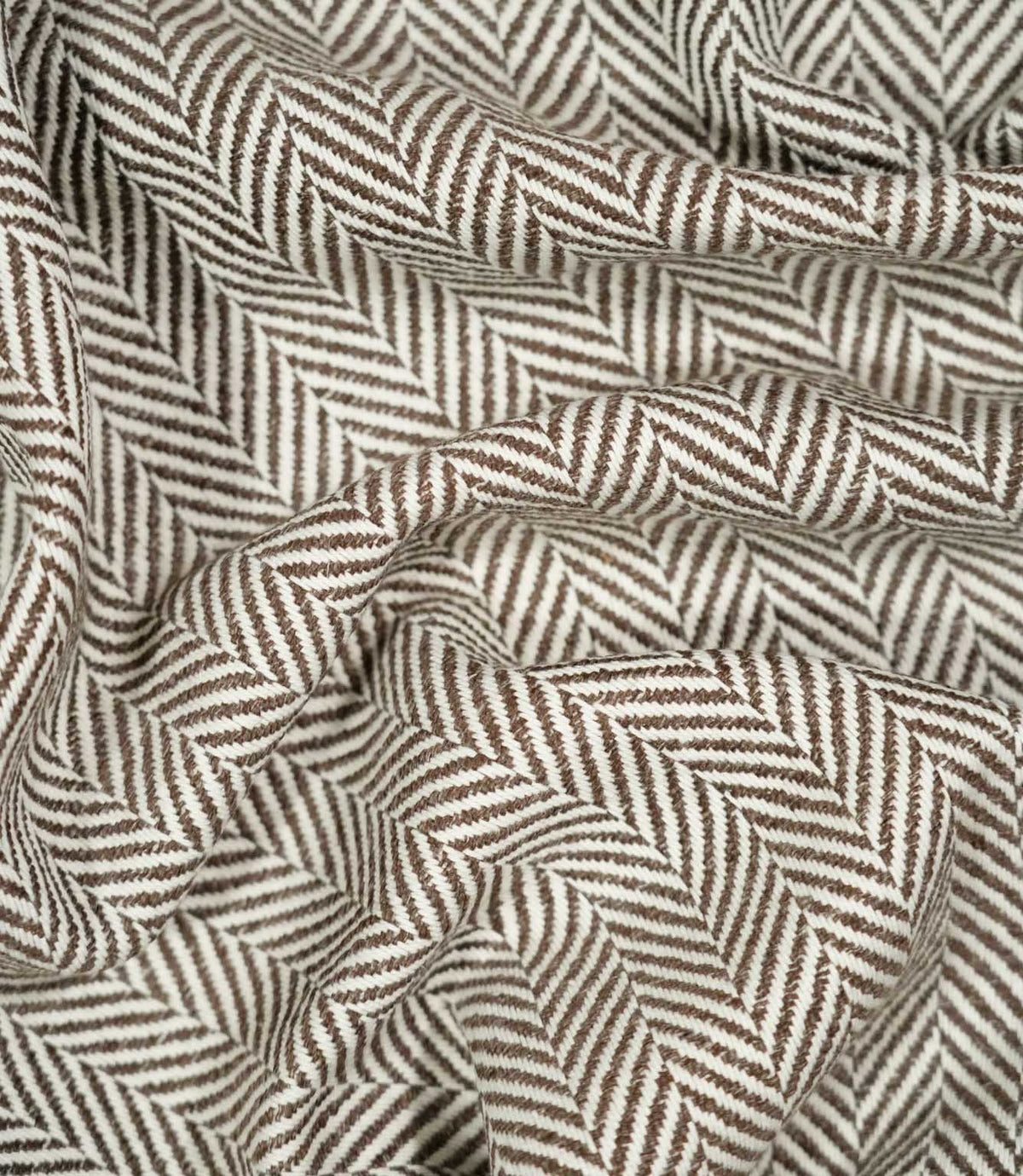 Bampton Bison herringbone fabric loosely draped and gathered, demonstrating the natural movement of the material and its distinctive brown and off-white herringbone pattern.
