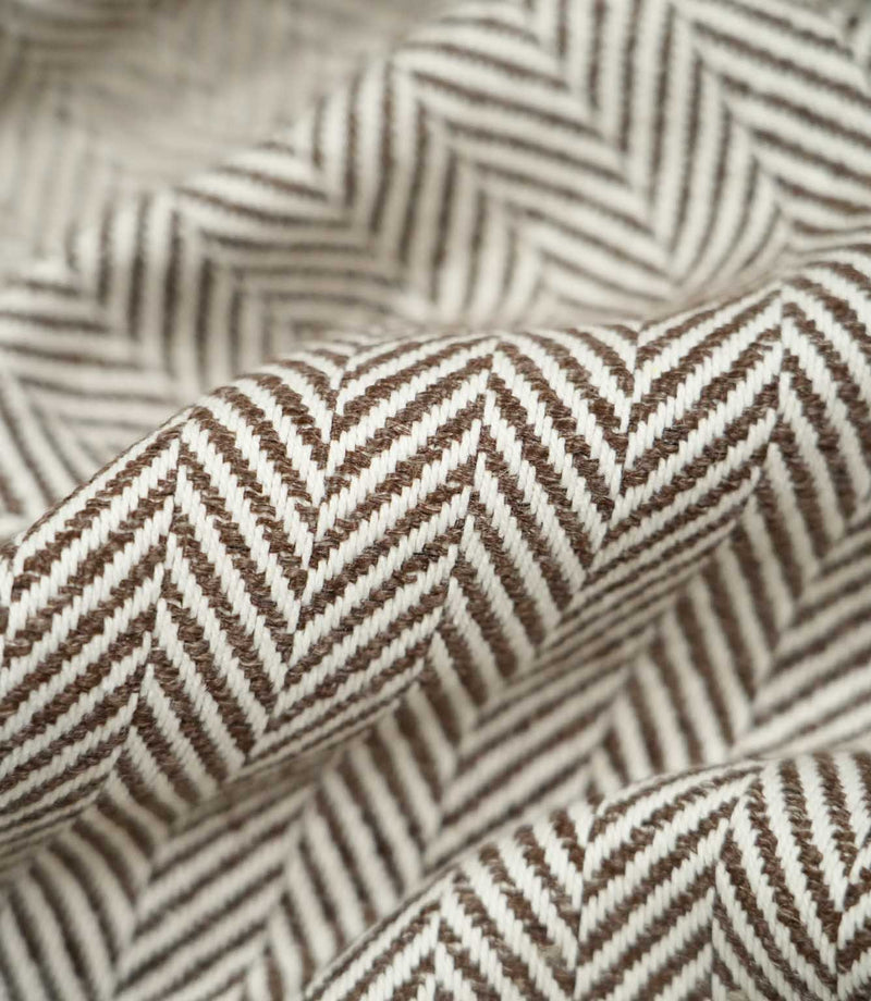 Macro close-up of draped Bampton Bison herringbone fabric, highlighting the individual woven fibres, raised texture and detailed chocolate brown and off-white chevron design.